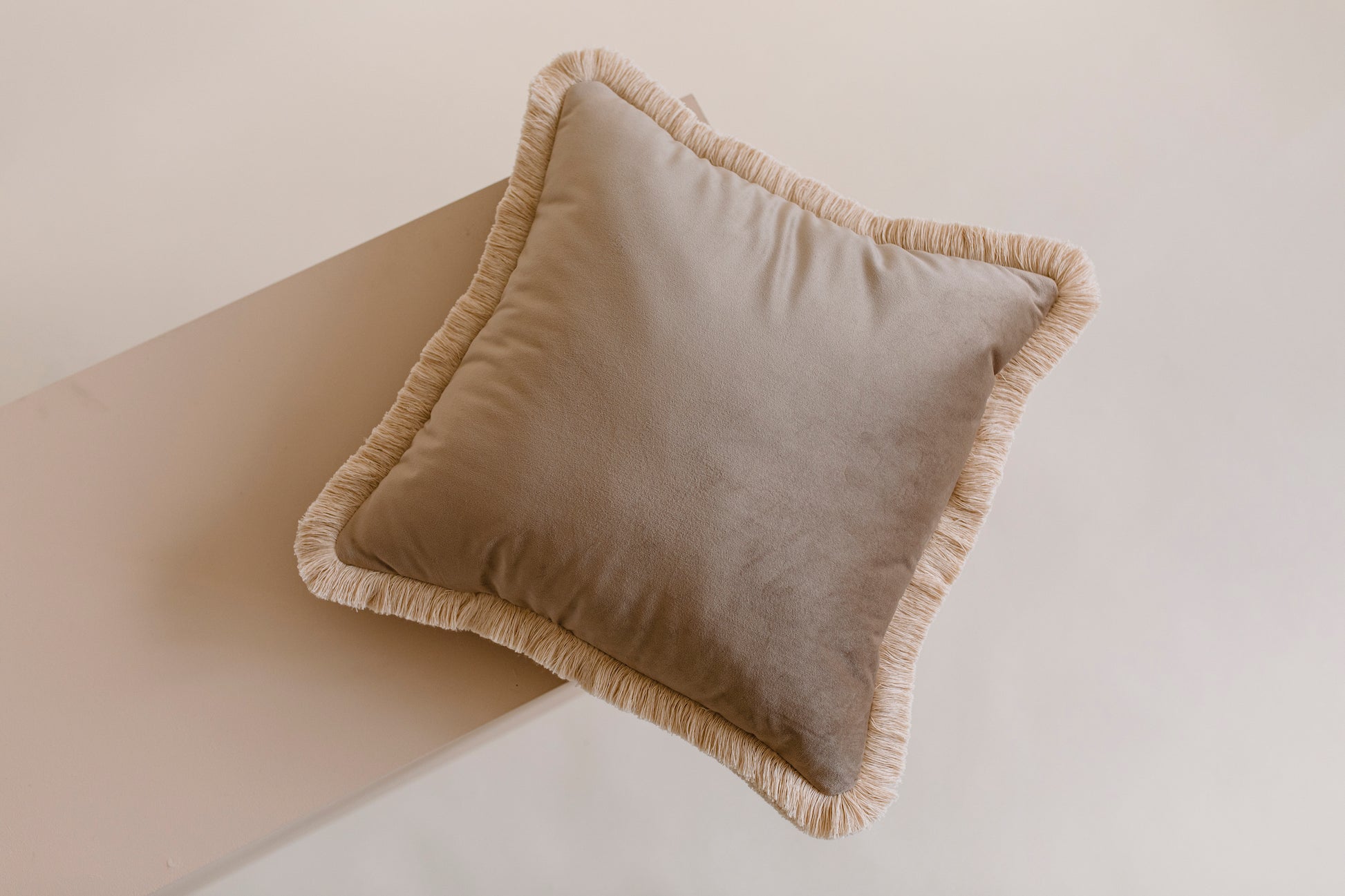 brown velvet cushion with a cotton fringe on the floor