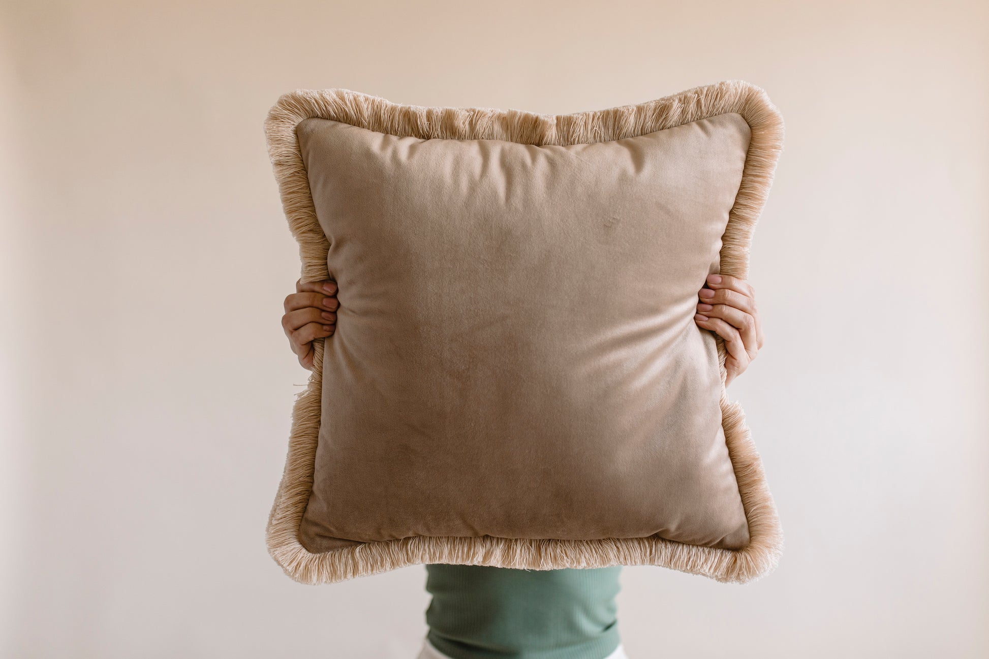 a girl holding big brown velvet cushion in front of her